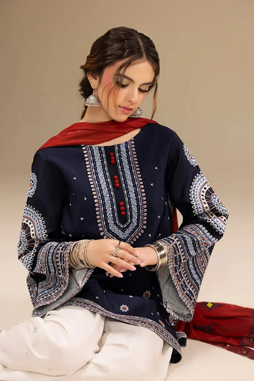 Woman wearing a navy blue embroidered top with white pants and a red scarf on a beige background