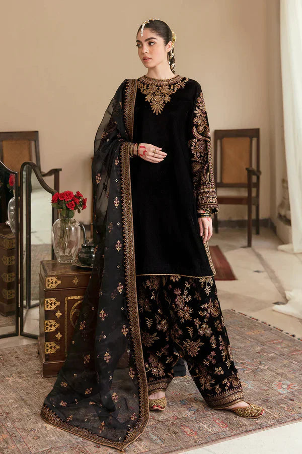 Woman in traditional black and gold outfit with dupatta in a decorated room.