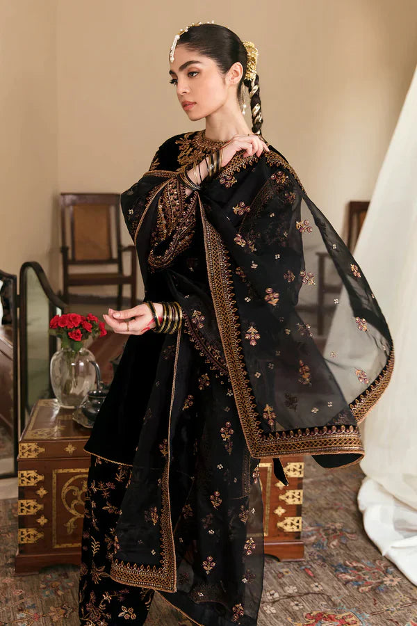 Woman in traditional black embroidered outfit with gold details in an indoor setting.