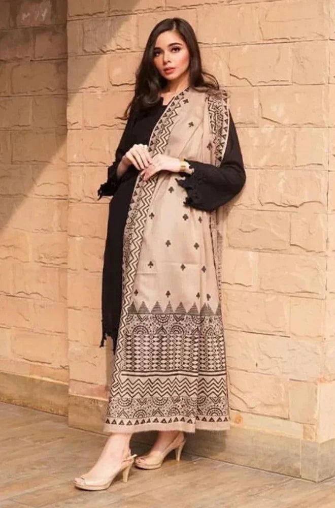 Woman wearing a patterned dress and black jacket against a stone wall.