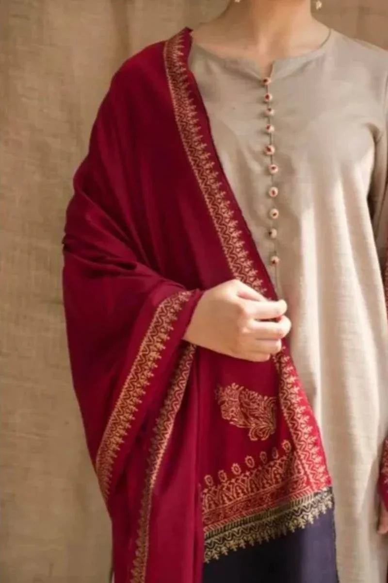 Person wearing a red shawl with gold embroidery over a light gray top on a beige background